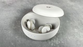 The Soundcore Sleep A30 earbuds are in their charging case. The three indicator lights on the front of the case are lit up white.