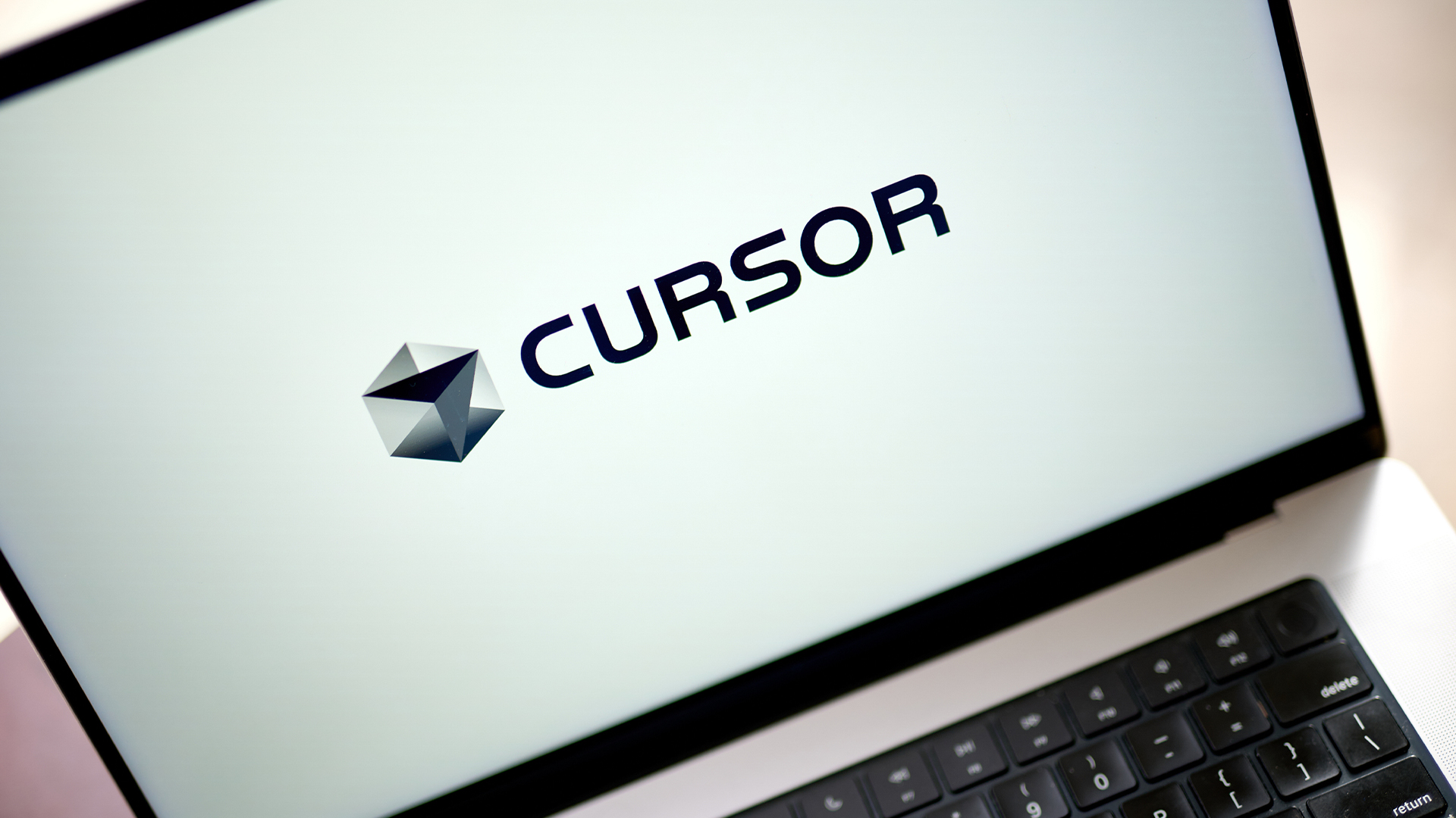 Logo of vibe coding startup Cursor pictured on a laptop screen placed on a desk.