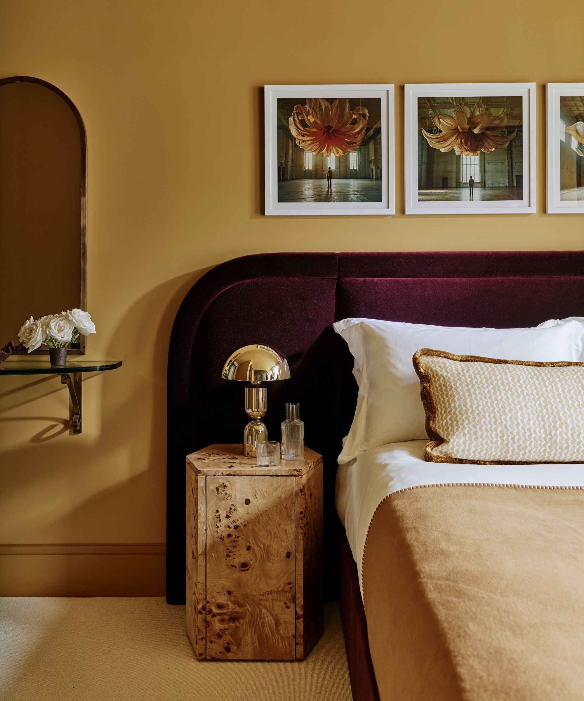 dark yellow bedroom with carpeted floor, burgundy purple velvet headboard, white and camel bedding with a burl wood side table