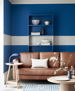 A living room in true blue 'Mazarine' by Little Greene, with accent white stripe, brown leather couch and light colored wood coffee table