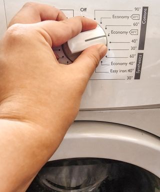 A hand turning the dial on a white washing machine with a t-shirt in the drum