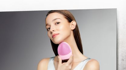 A woman looking in the mirror using the best facial cleansing brush, the Foreo Luna 3