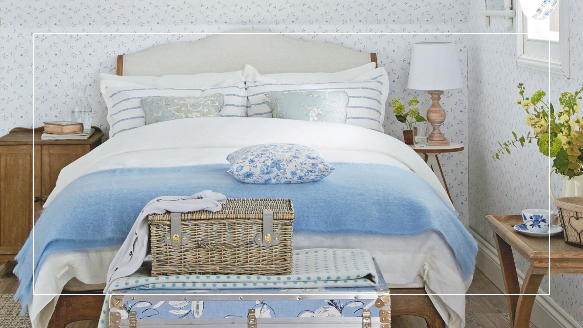 pale blue and white bedroom with an upholstered linen bed and wicker hamper on an ottoman at the foot of the bed