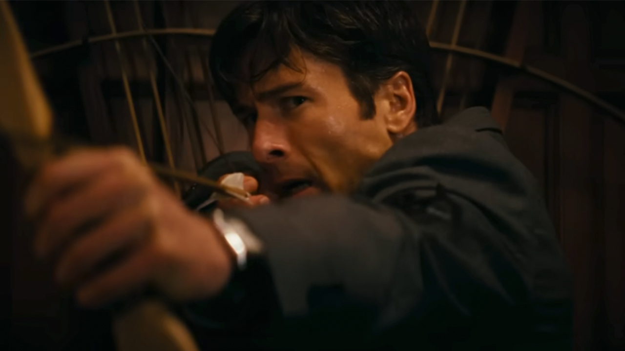 A close up of Glen Powell aiming a bow and arrow in How To Make A Killing