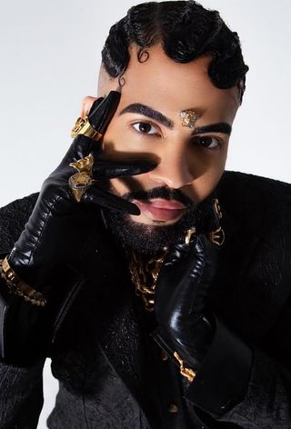 a headshot of the celebrity stylist, Mickey Freeman wearing black leather gloves, gold jewelry, and a black blazer