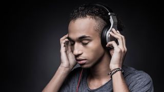 Side view of young man adjusting headphones and keeping eyes closed