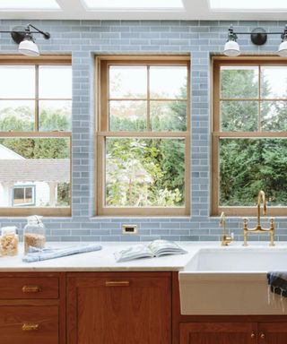 A blue tile kitchen with windows, a sink, and wooden cabinetry