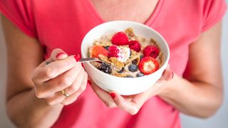 Woman holds spoon of cereal packed with fiber up from a bowl