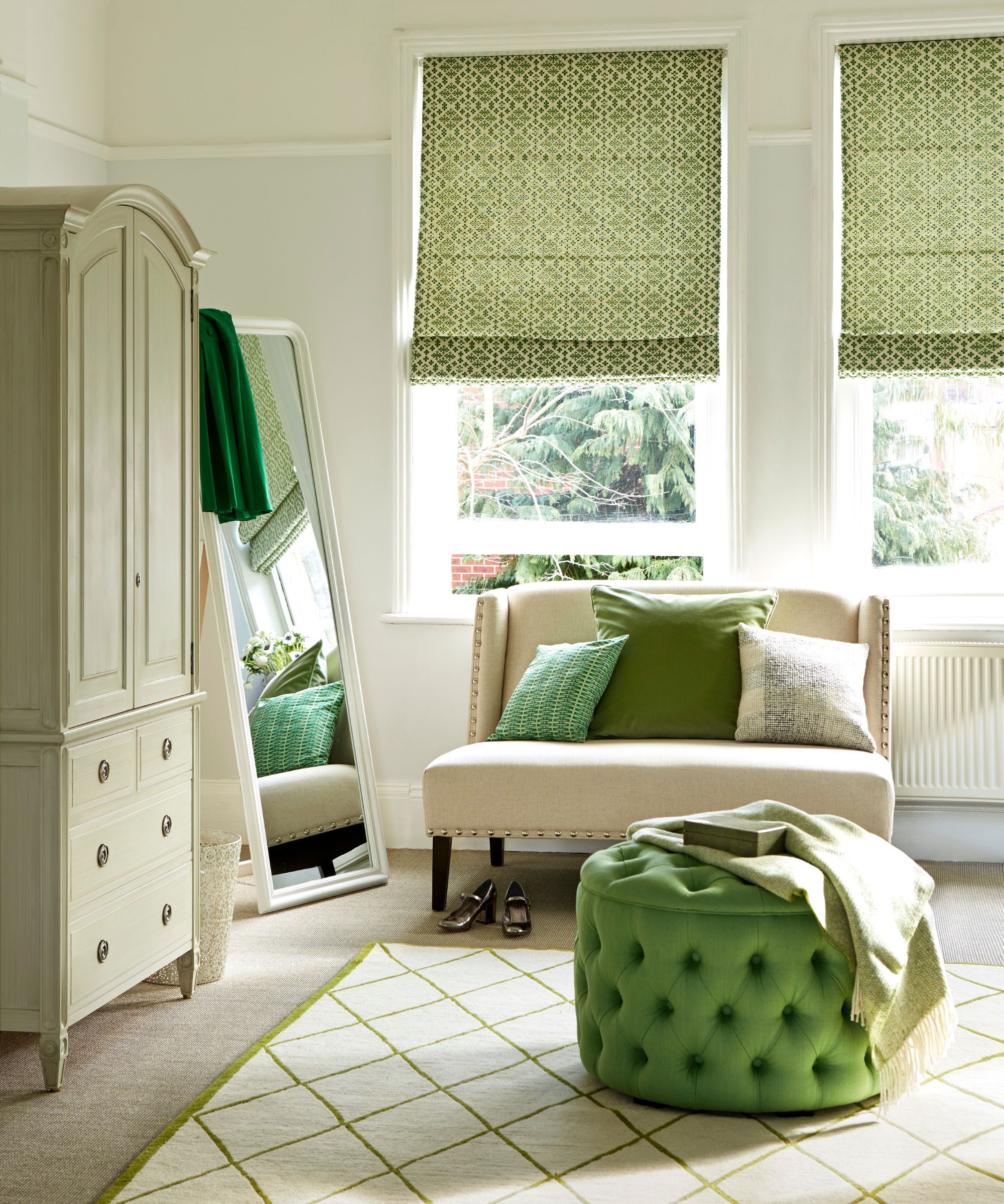 A green bedroom with a cream carpet, pale green closet, white full-length mirror, white couch with green cushions, a white and green patterned carpet, and a green storage ottoman.