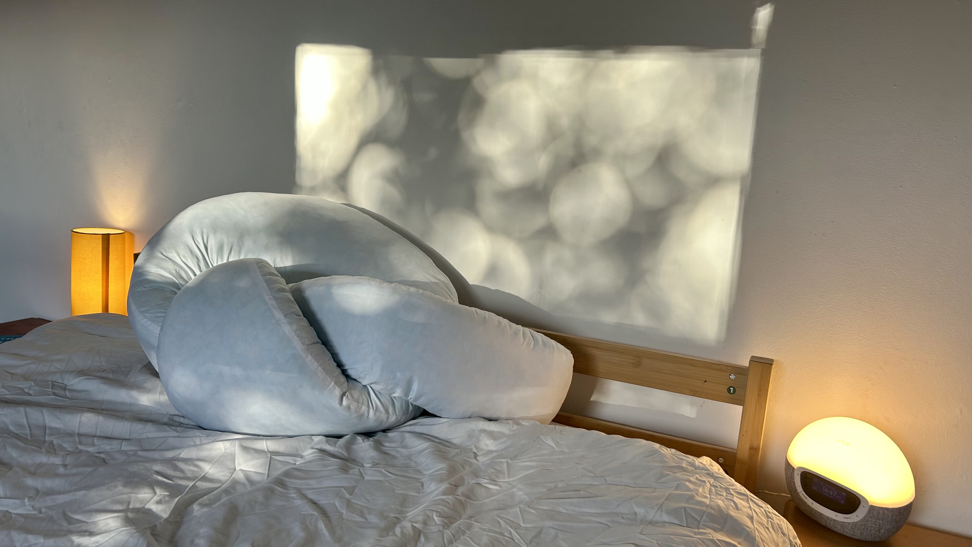 The Yana 360&amp;deg; Body Pillow folded into a tight knot on a bed with white bedding.
