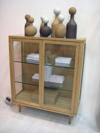 Glass and wood cabinet with bottle -like sculture displayed on the top, photographed against a white background