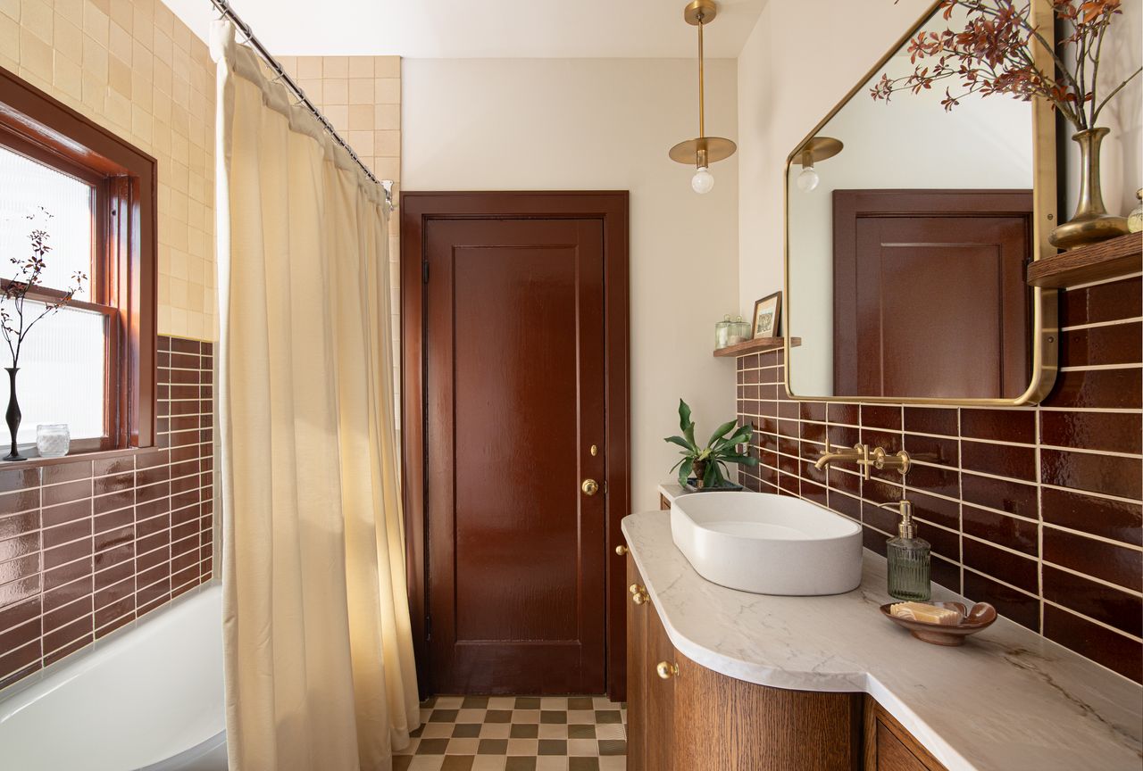 Bathroom with dark red tiles, checkerboard floor, gold mirror and light, marble countertop
