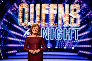 Lorraine Kelly stands in the Queens For The Night studio in front of a screen displaying the show's logo