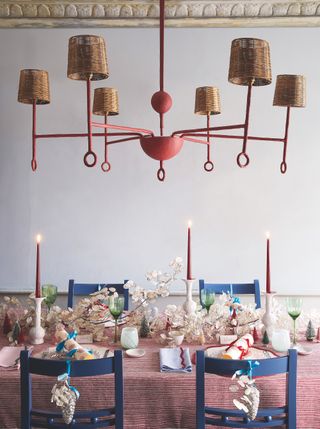 Christmas table with table laid for dinner with lit candles, Christmas crackers, honesty garland, brightly coloured tableware, large central lamp above