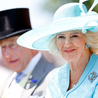 Queen Camilla in a turquoise hat and coat sitting next to King Charles
