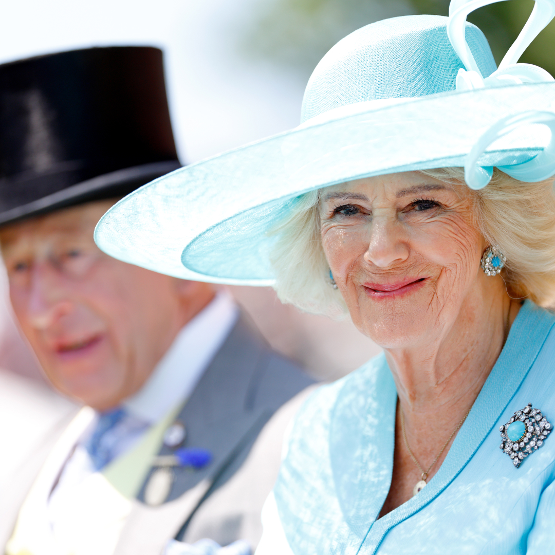 Queen Camilla in a turquoise hat and coat sitting next to King Charles