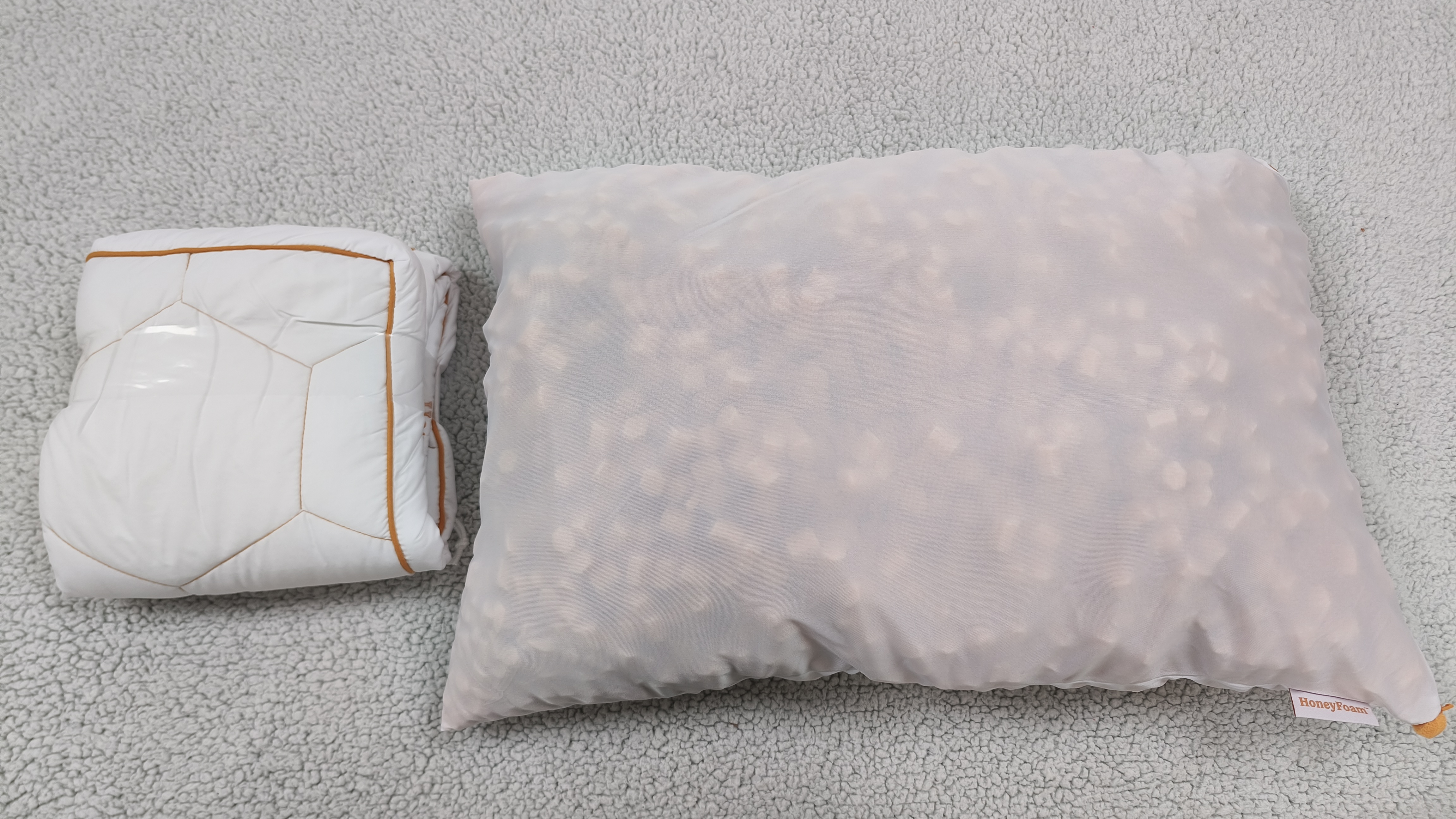 A white quilted pillow cover folded next to a semi-transparent mesh inner bag filled with orange foam clusters, both resting on a textured gray surface.