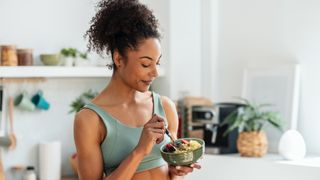 Woman eating a bowl of food in a light and airy kitchen wearing a sports bra