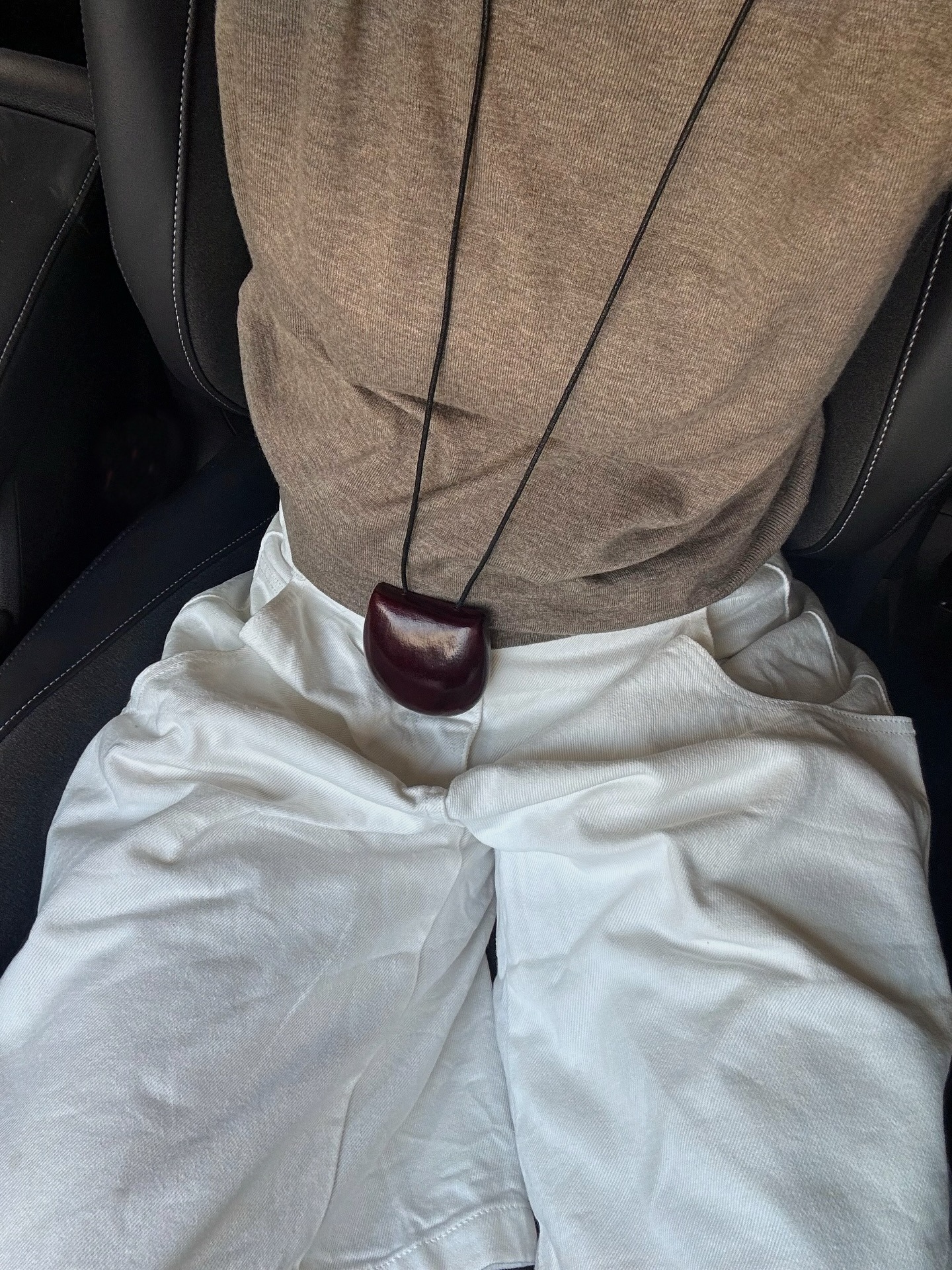 Linda Tol wearing a burgundy pouch purse over a brown sweater and white pants.