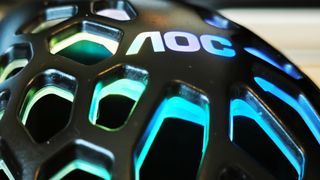 A black AOC GM510 gaming mouse with a hollow honeycomb structure and RGB lighting sitting on a desk
