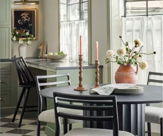 Green and cream kitchen with dining table, decorated with ceramic vase and wooden candle holders