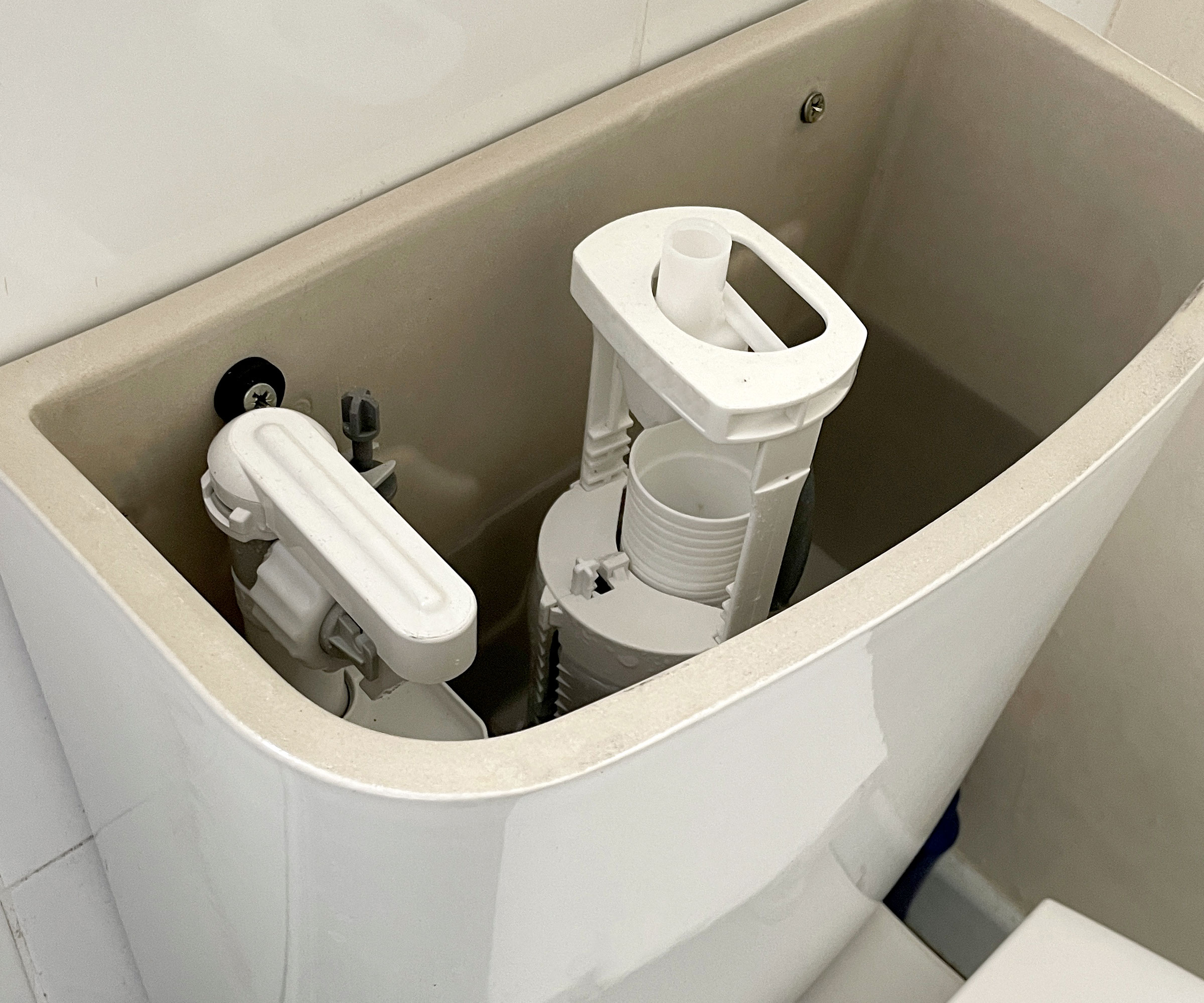 White toilet cistern/tank with lid off, showing inlet valve and flush valve unit