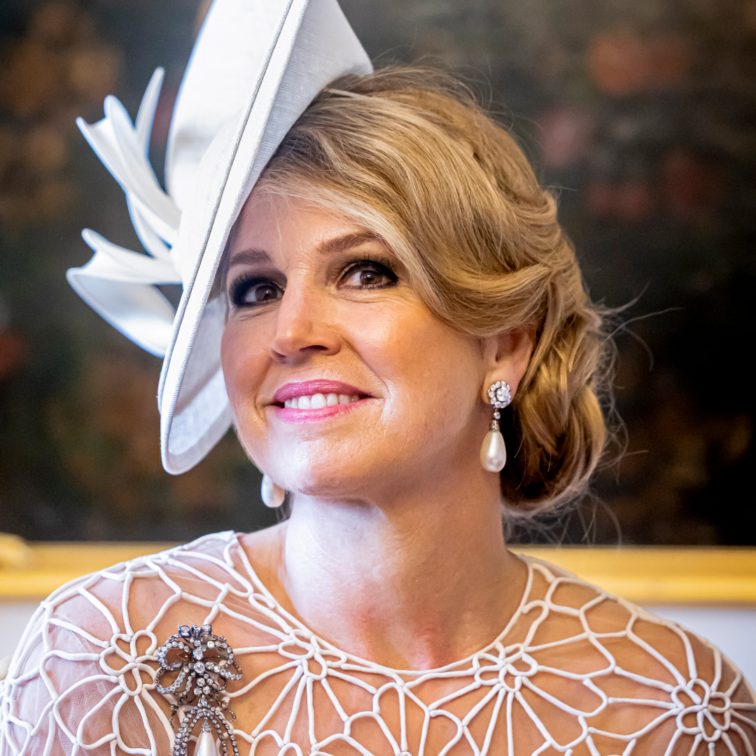 Queen Maxima wearing a white hat and lace dress with pearl earrings