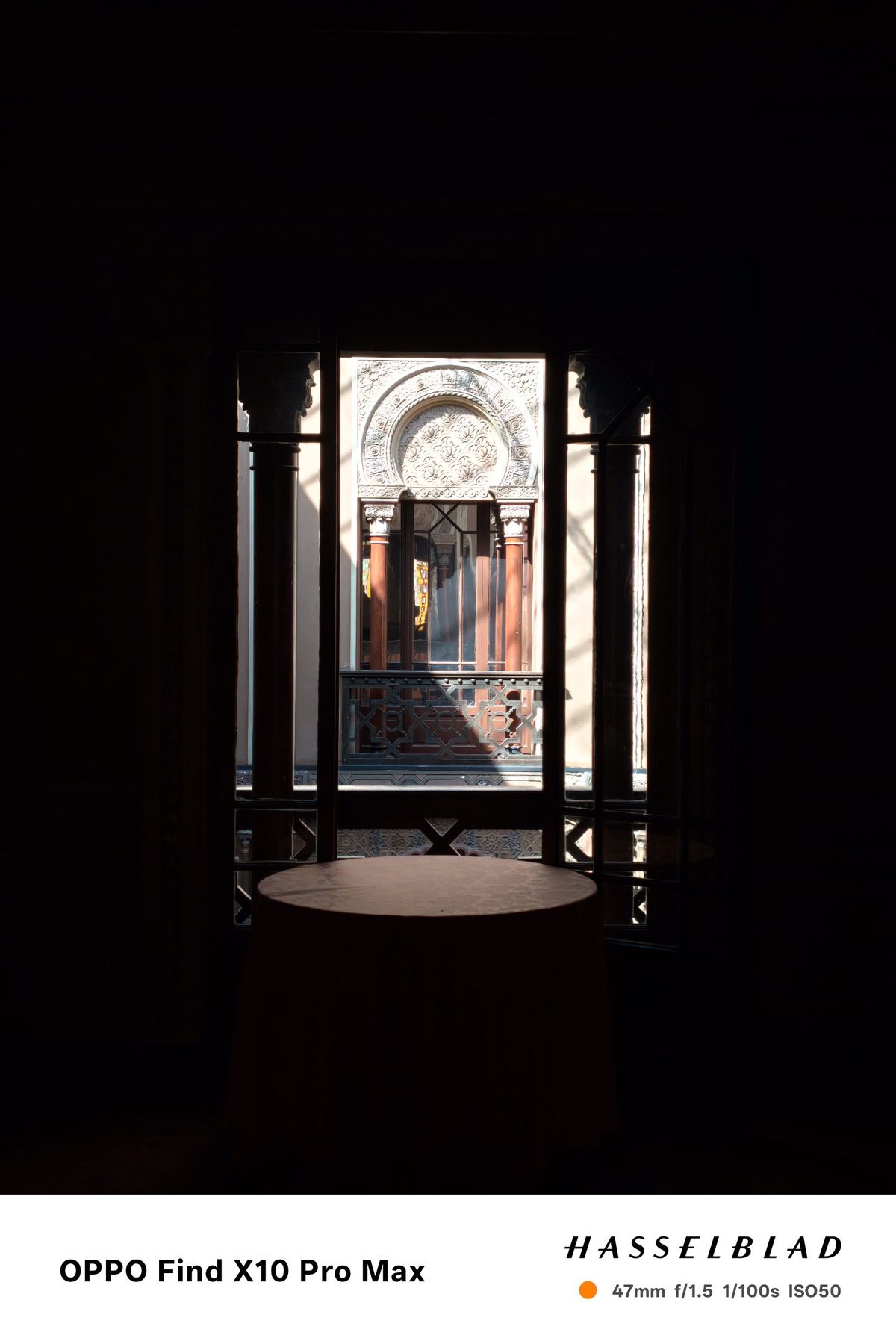Ornate courtyard window framed by a dark interior, with bright sunlight outside.