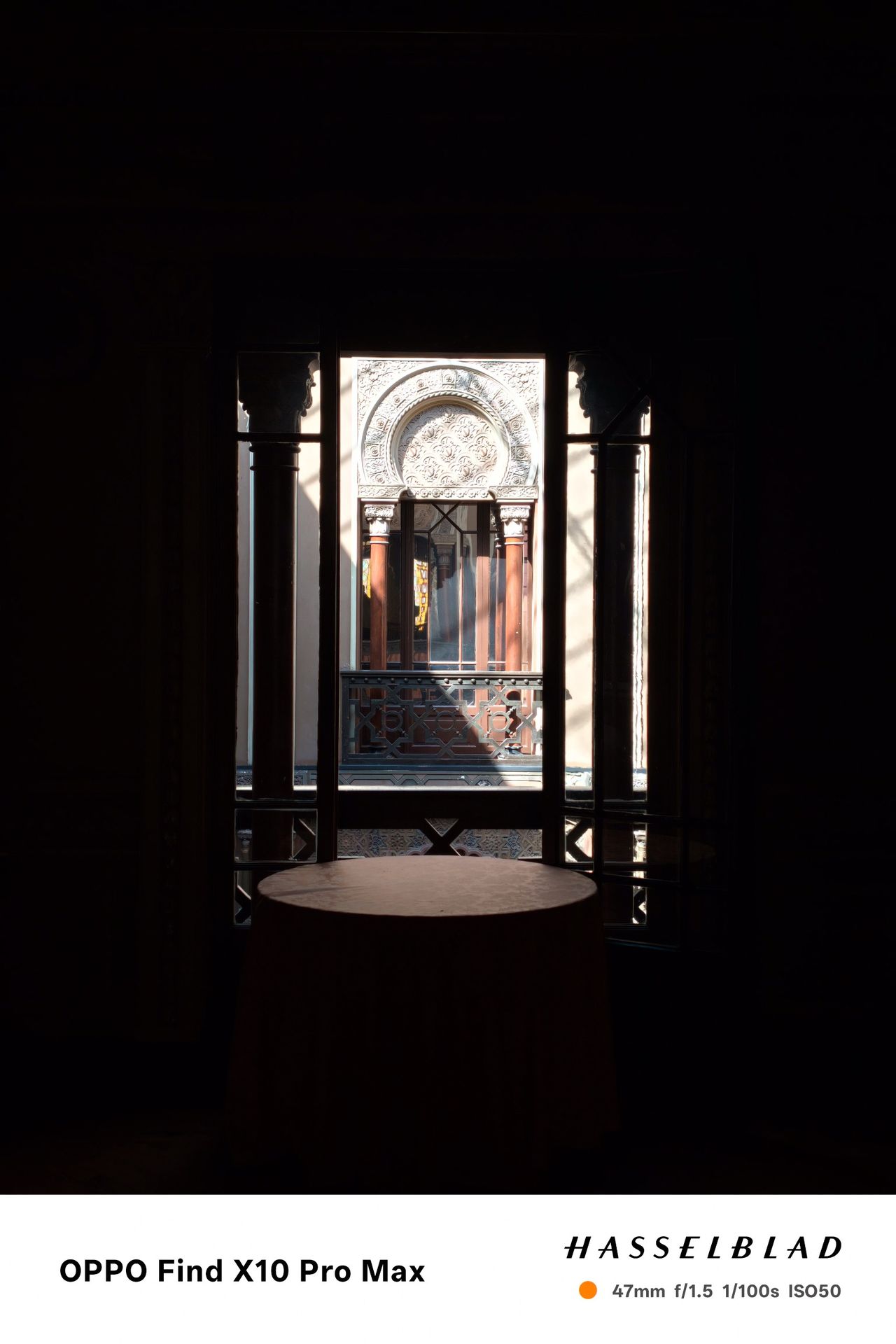 Ornate courtyard window framed by a dark interior, with bright sunlight outside.