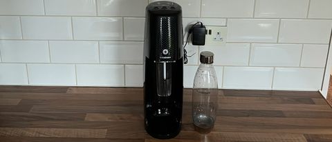 The Sodastream Spirit One Touch on a kitchen countertop next to the plastic water bottle its bundled with