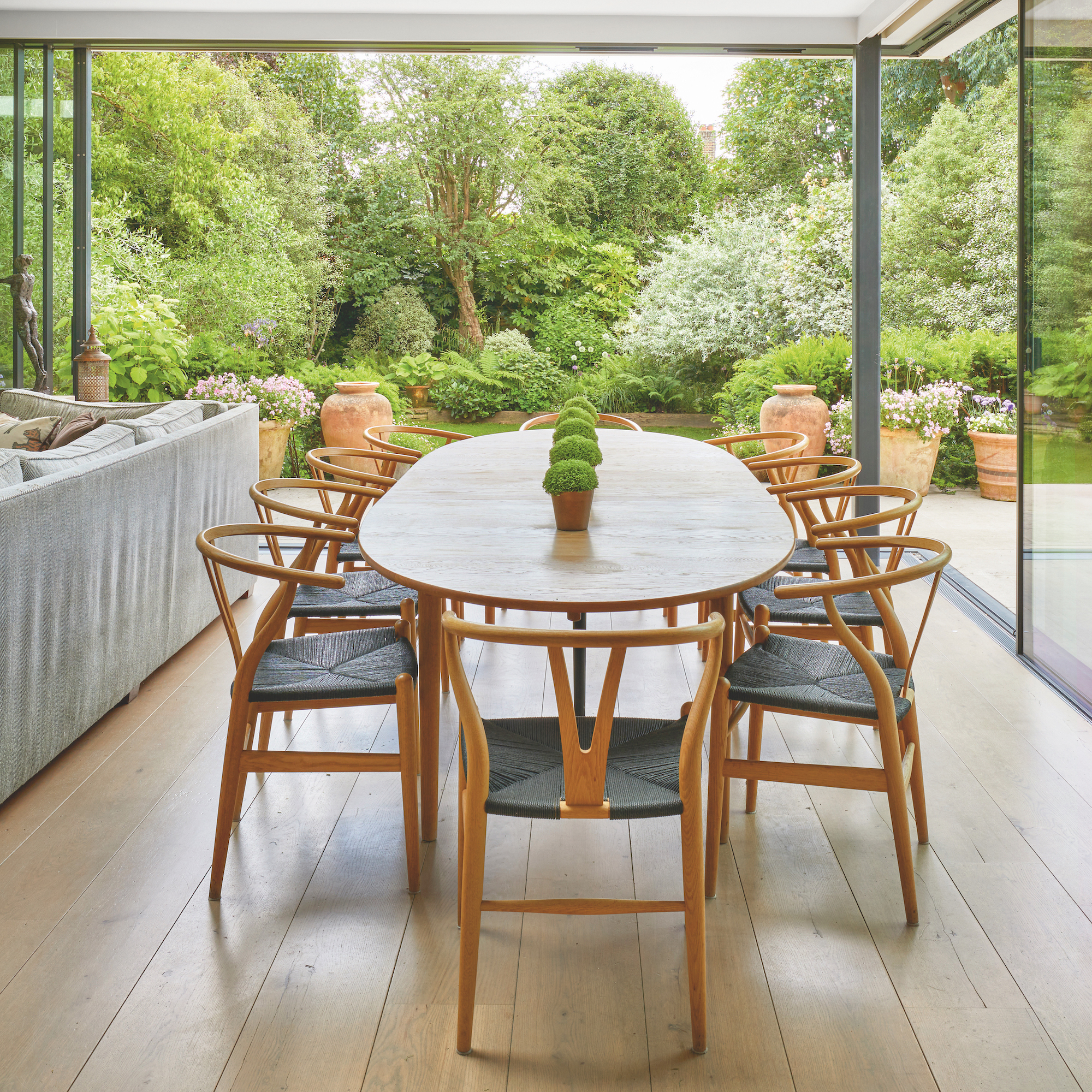 dining area in open plan living area with floor to ceiling glazing and wooden table with wishbone dining chairs
