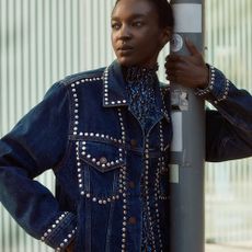 Young woman wearing denim jacket with rhinestones leaning on lamppost 