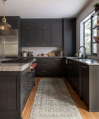 modern kitchen with dark charcoal cabinets and island, light gray rug, brass accents and pendant light