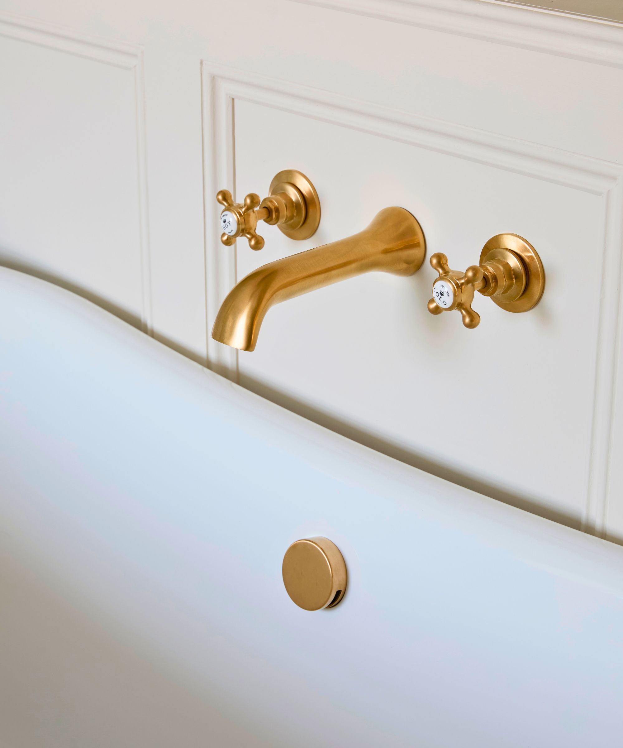 Traditional brass wall-mounted bath tap with cross handles over a freestanding bath.