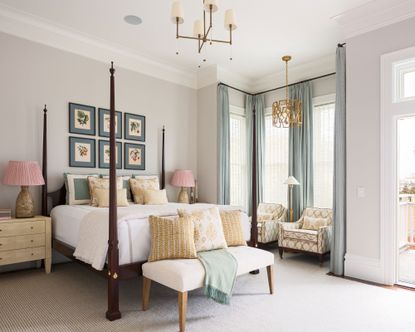 Large master bedroom with gray painted walls, cream carpet, dark wood four poster bed, blue botanical artwork above bed, blue curtains, two unique pendant lights, one above bed, one above two armchairs beside the window