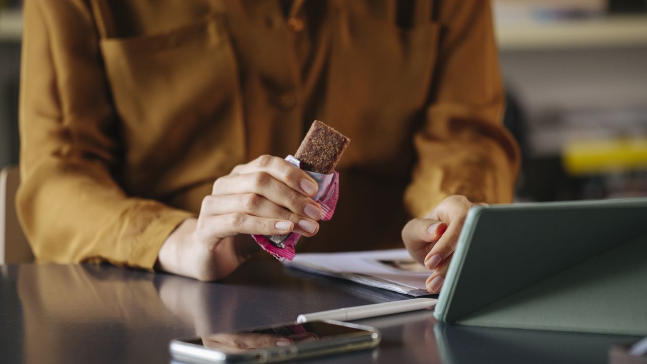 woman eating a protein bar at her desk