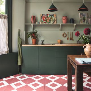 two tone green painted kitchen with open shelving, pink and white patterned painted flooring, table, striped curtain at window, pendant lights