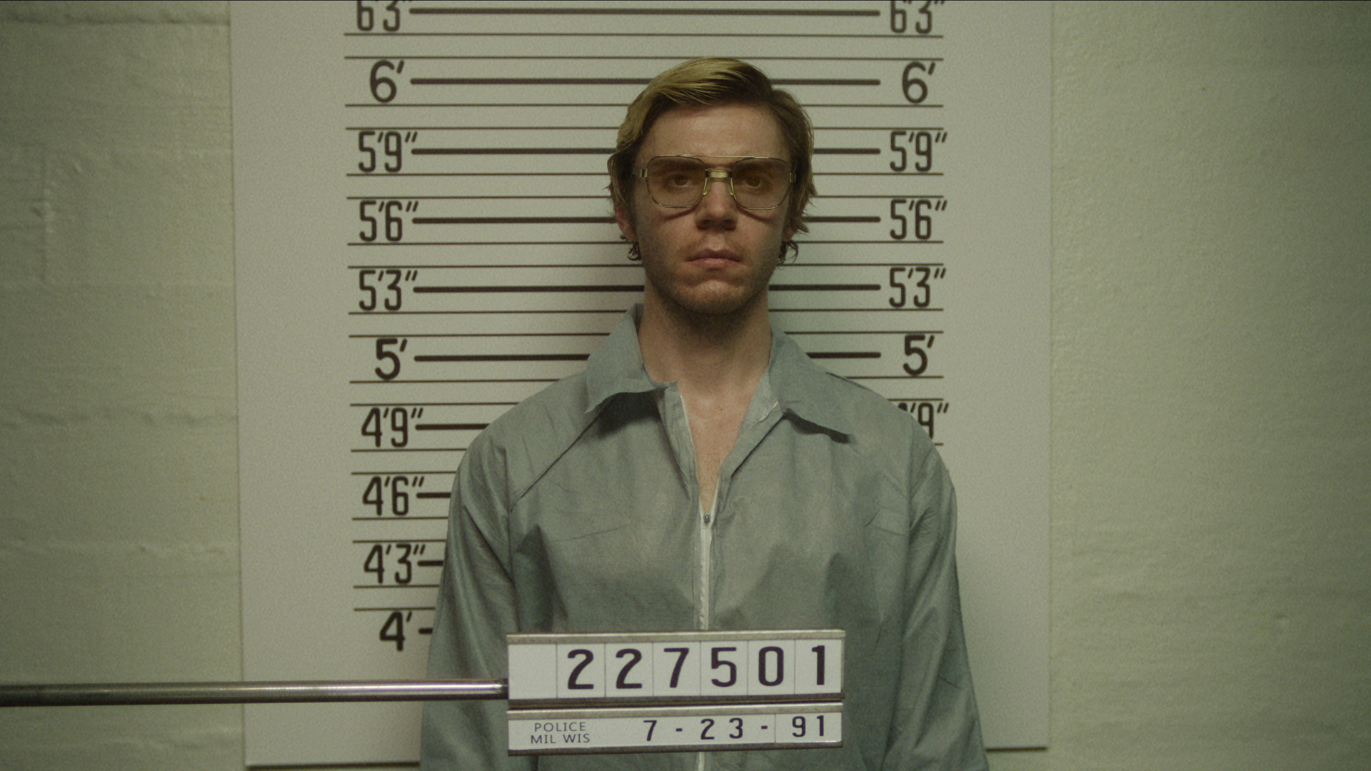 Jeffrey Dahmer von Evan Peters steht vor einer Messwand, während sein Polizeifoto in Monster: The Jeffrey Dahmer Story aufgenommen wird