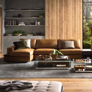 Tan leather corner sofa in a large grey living room with vertical wooden wall panelling and open shelving