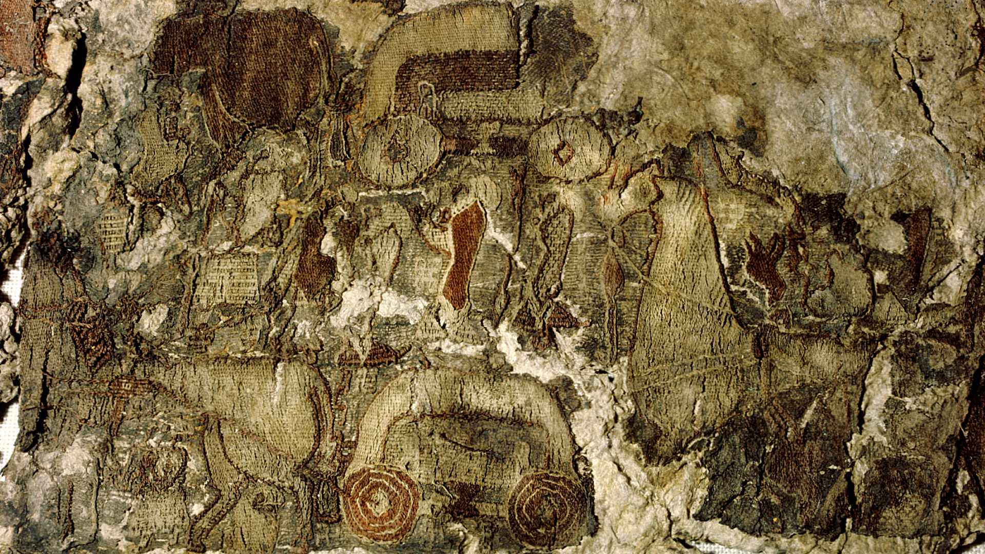 Fragment of a tapestry in beige and brown colors showing wheels and a dress in red
