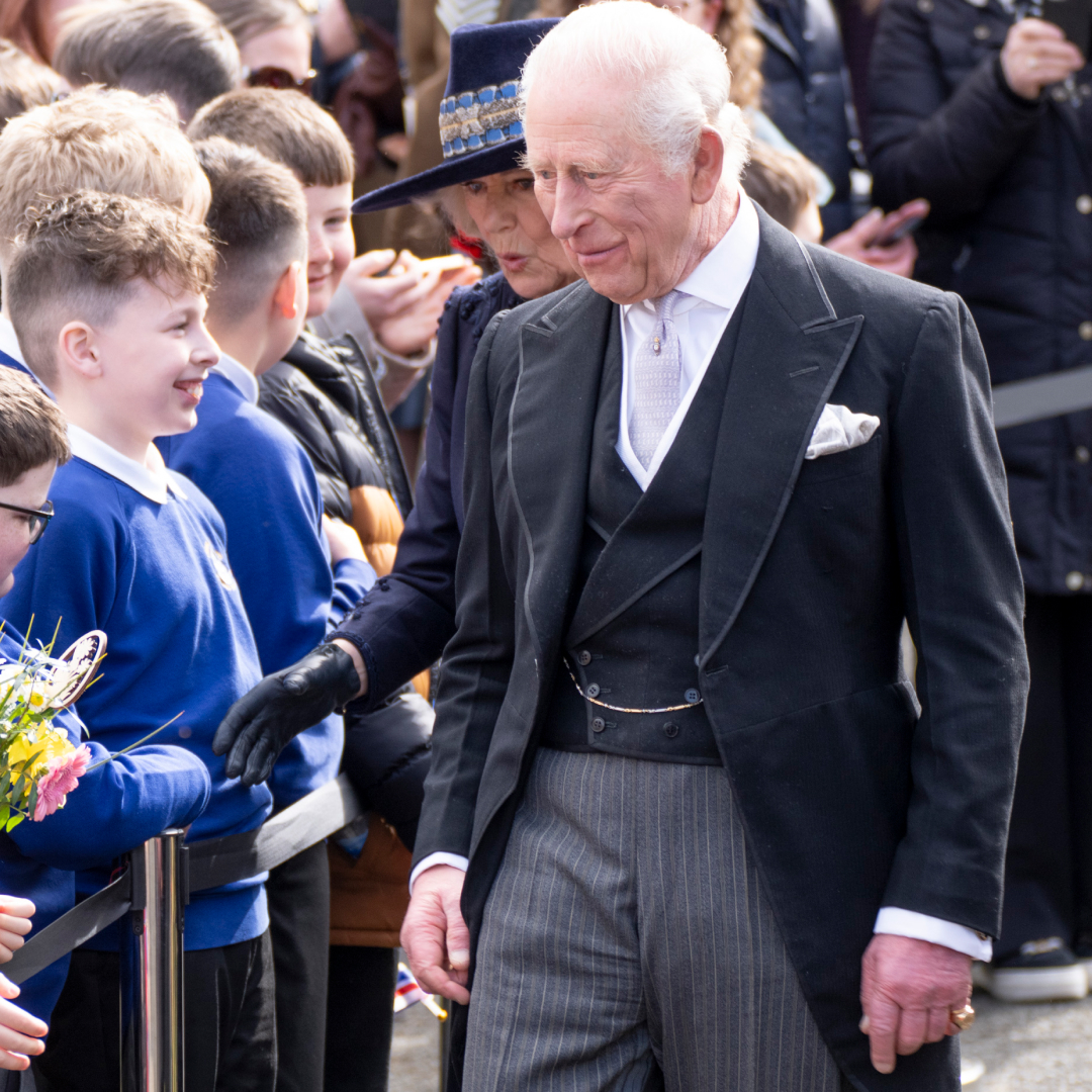 King Charles wearing a suit walking past a group of students