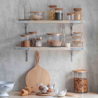 A grey kitchen with pale wood open shelving and glass storage jars