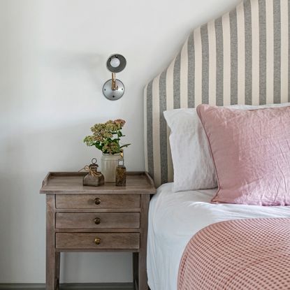 Bed with striped upholstered headboard and small wooden nightstand