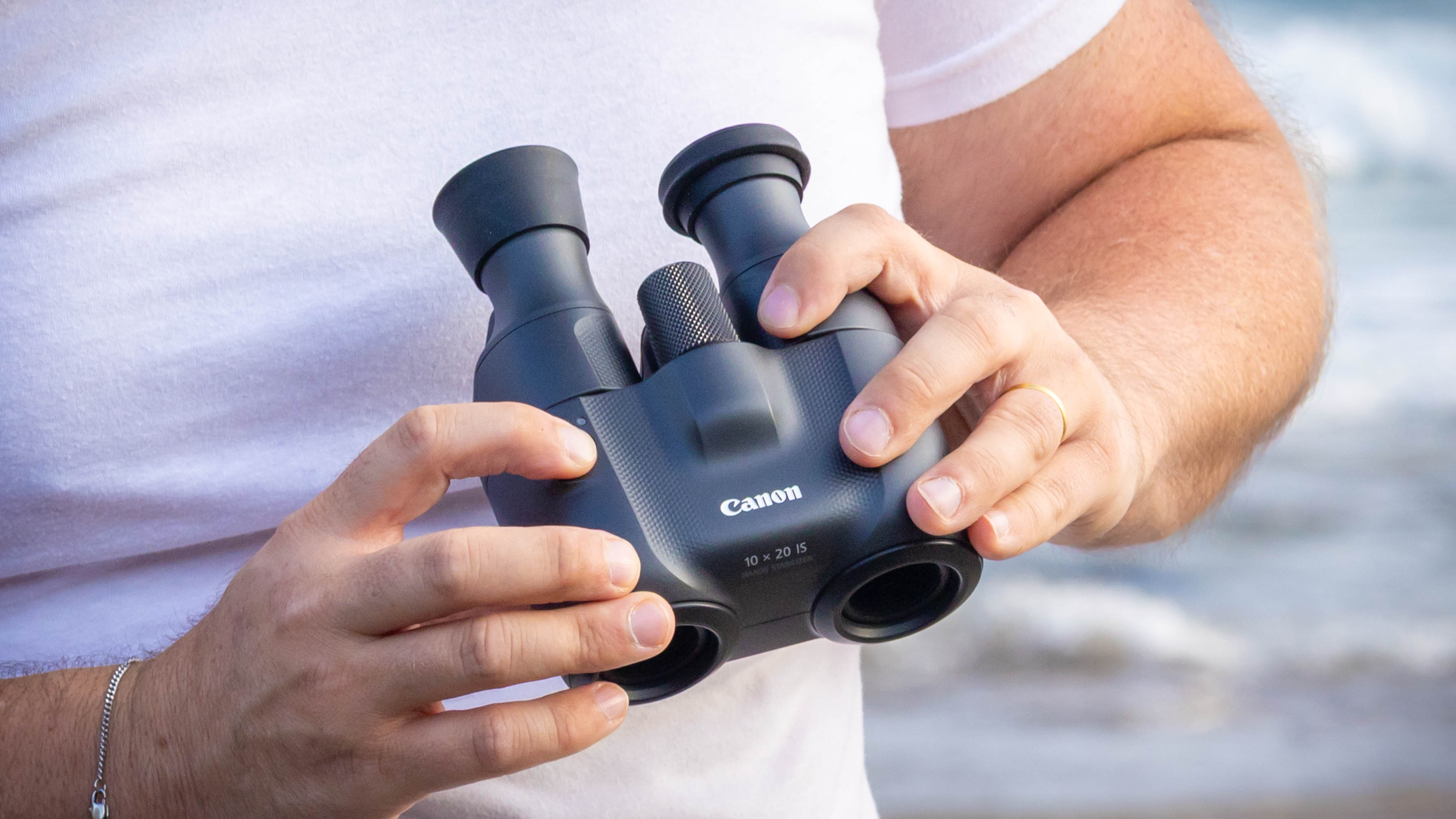 A close-up of the Canon 10x20 IS binoculars being held by a person.