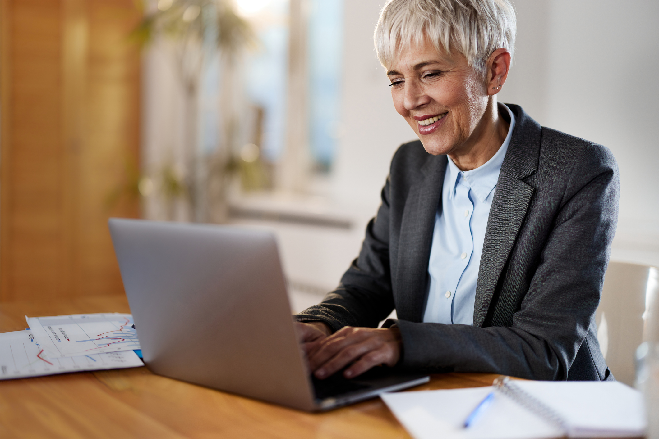 Happy senior businesswoman working on laptop at home office.