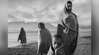 Draped in blankets to keep out the cold morning wind, refugees wait outside Korem camp. Ethiopia, 1984. © Sebastião Salgado