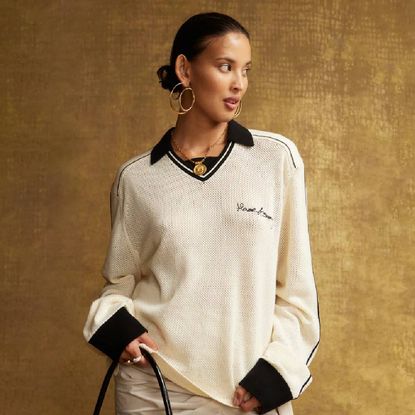 A woman wearing a cream and black knit from House of Sunny in front of a brown backdrop.
