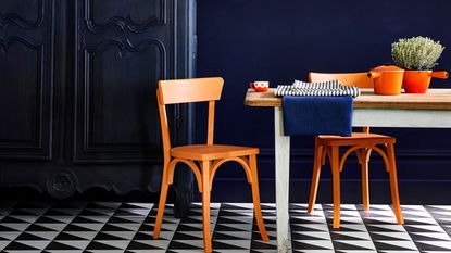 An Annie Sloan lifestyle image featuring some the best paint for furniture including Oxford Blue on armoire and Barcelona orange on wooden dining chairs