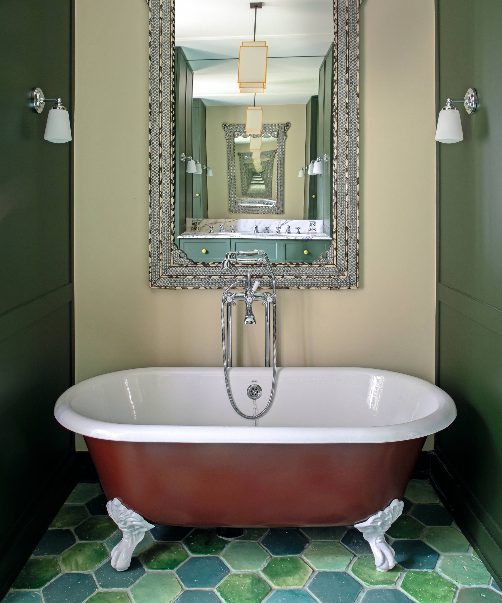 a bath nook with dark green walls either side with a dark red claw foot bathtub, green hexagon floor tiles and a large antique mirror