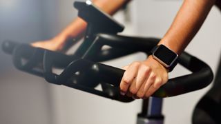 Image of woman using exercise bike with fitness tracker on wrist 